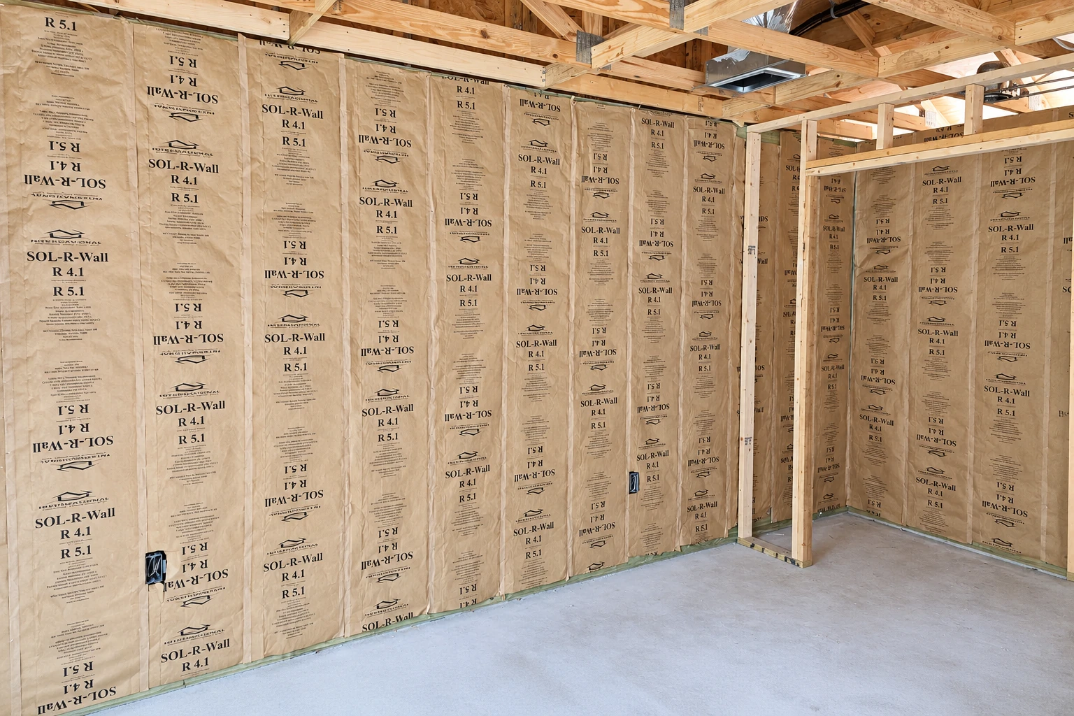 Commercial wall insulation with tan-faced batts fills exposed wooden framing in a large unfinished interior.