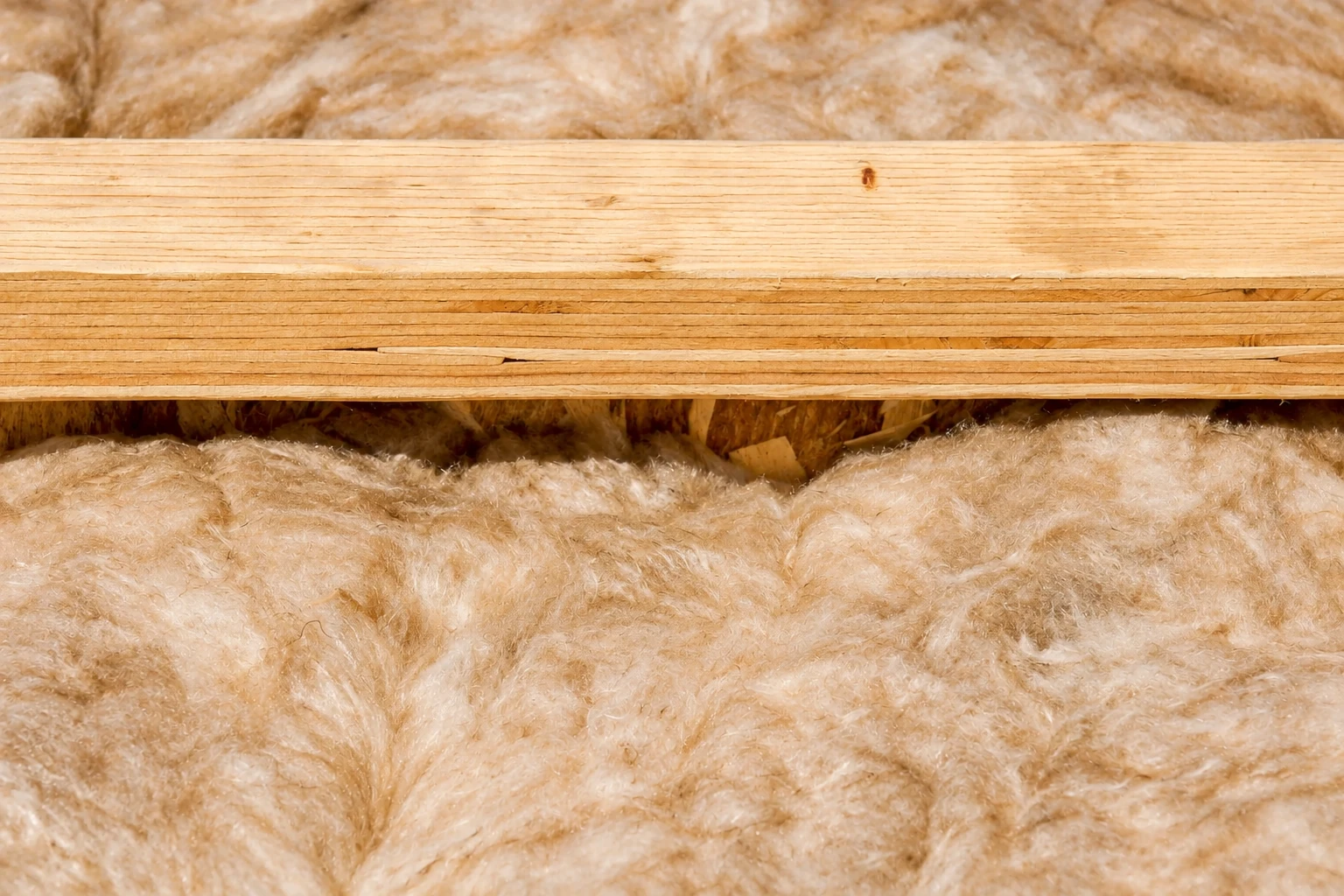 Close-up of tan fibrous batt insulation packed between wooden framing members.